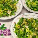 Three bowls of salad with a linen tablecloth background with purple embroidery flower pattern.