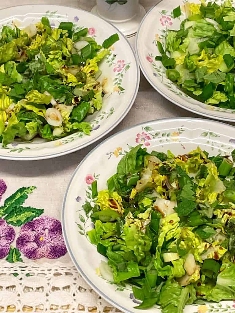 Three bowls of salad with a linen tablecloth background with purple embroidery flower pattern.