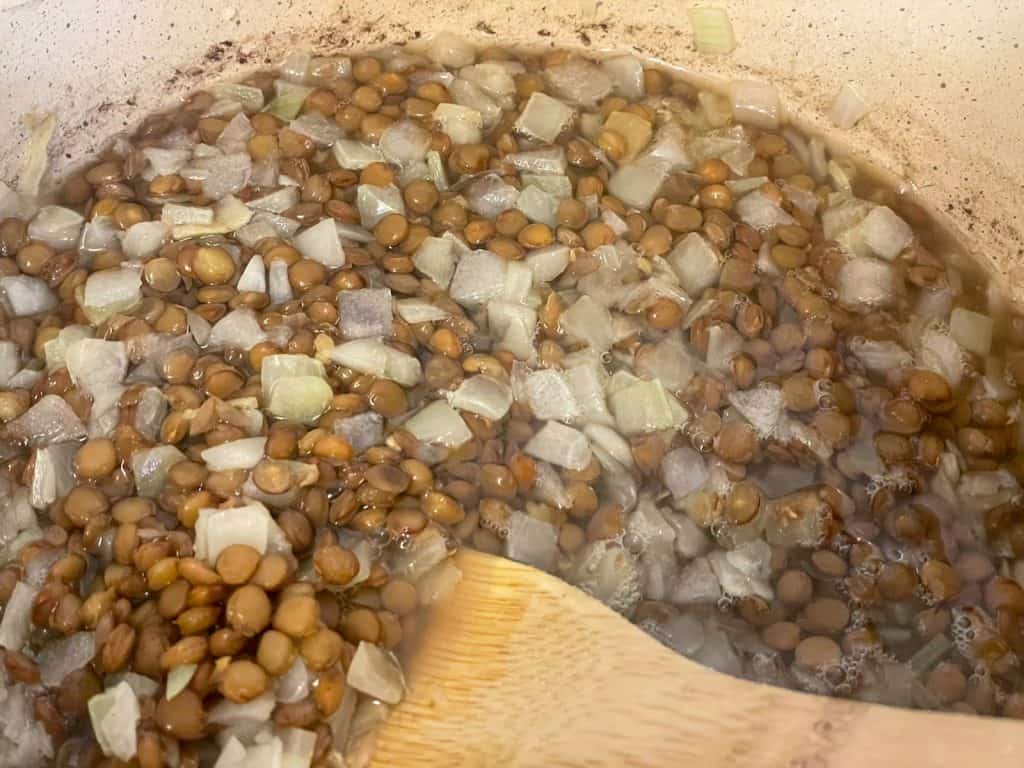 Onions added to green lentils in saucepan.