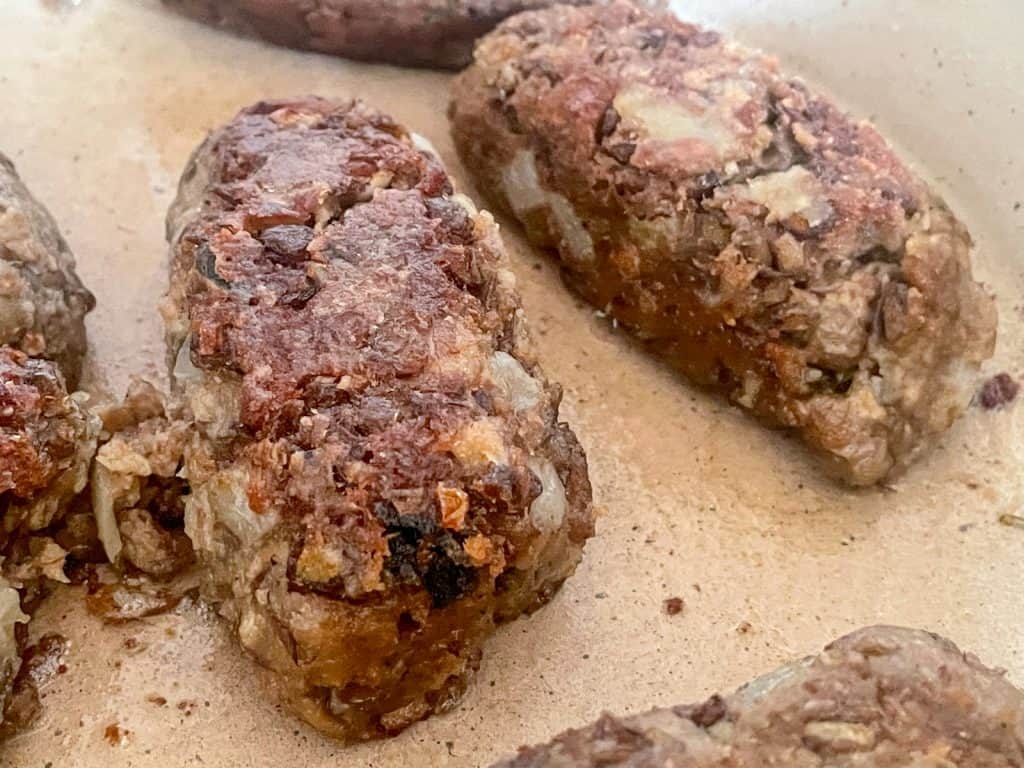 Lentil sausages cooking in pan.