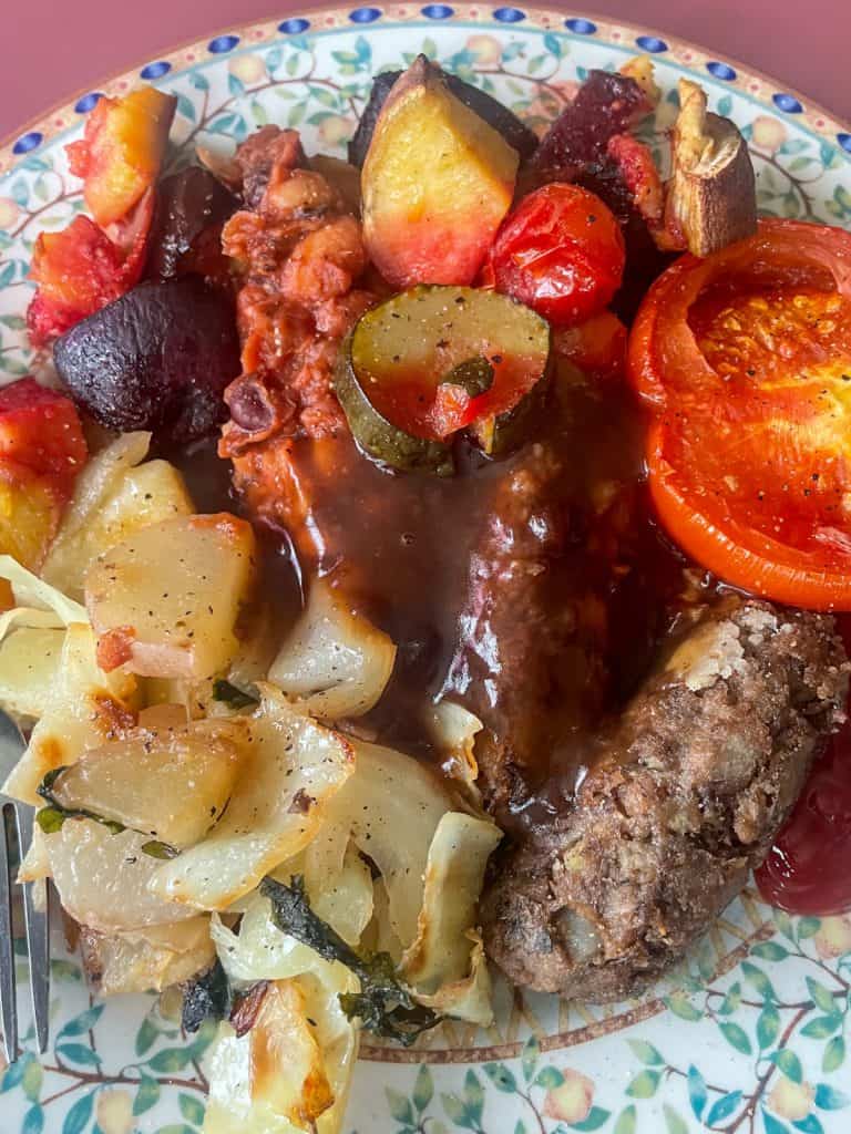 Green lentil sausages served on plate with gravy, roast vegetables, and fried potatoes and cabbage.