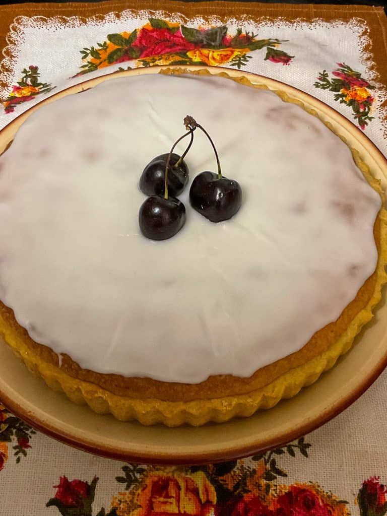 Unsliced Bakewell tart on a plate with a cherry garnish.