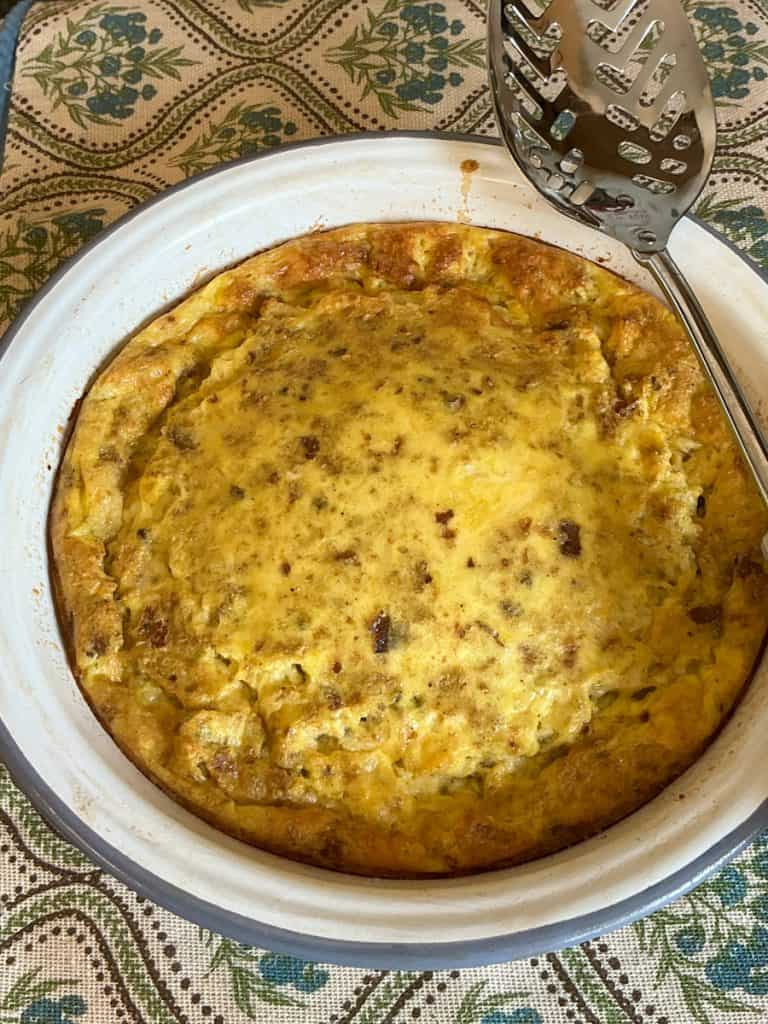 Cheese pudding baked and still in baking dish with a serving spoon to the side.