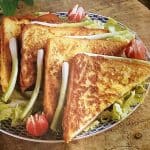 Creamy fried sandwiches on a plate with salad, brown table background.