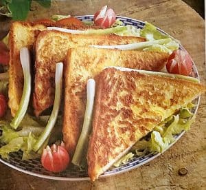 Creamy fried sandwiches on a plate with salad, brown table background.
