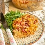 Serving plate with macaroni casserole and salad, casserole dish in background.