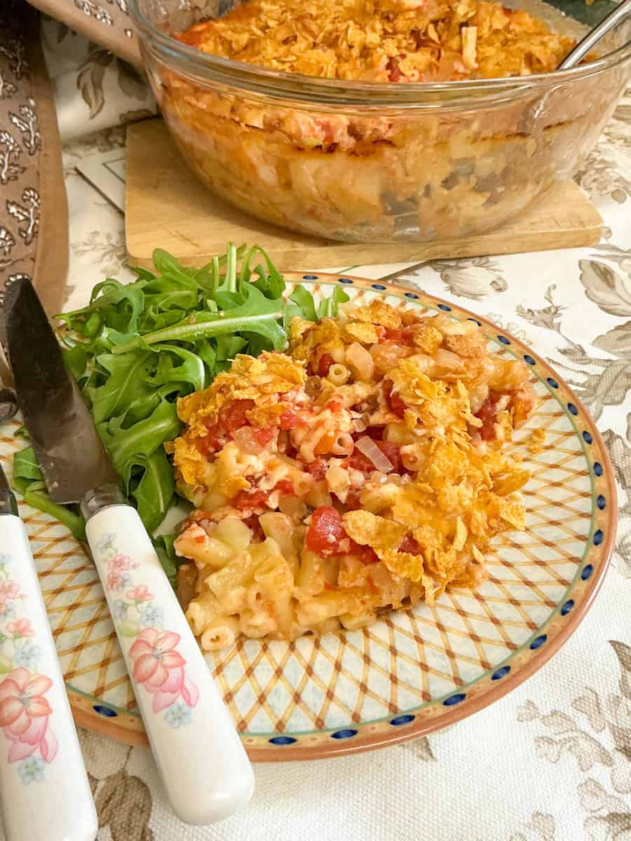 Serving plate with macaroni casserole and salad, casserole dish in background.